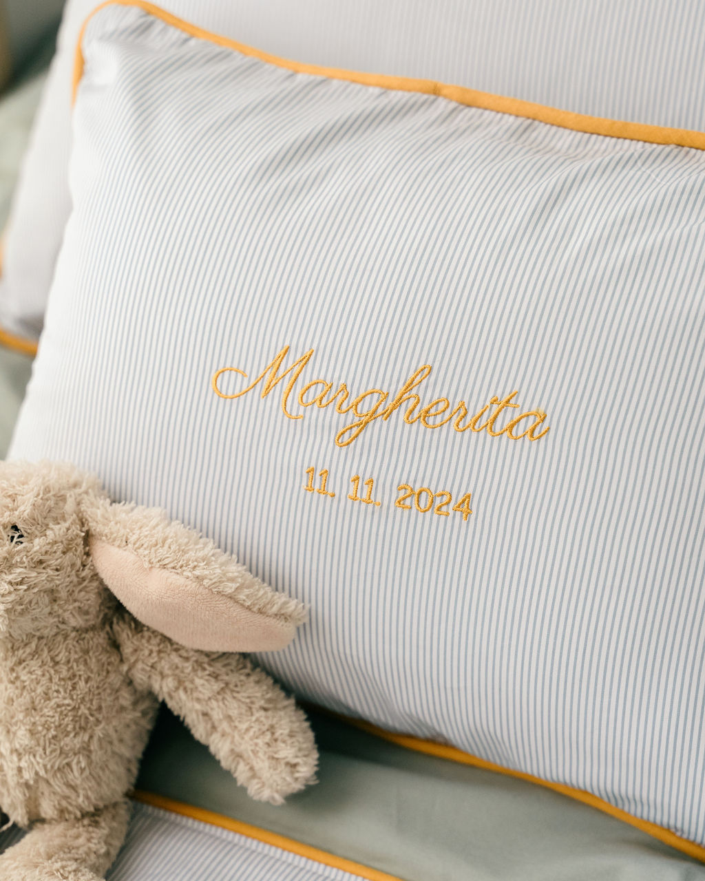 Blue pinstriped pillow with gold piping, an embroidered Margherita name and date, and a plush toy in front